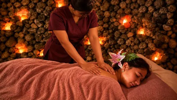 Masseurin bei einer Rückenmassage vor einer warm beleuchteten Steinwand